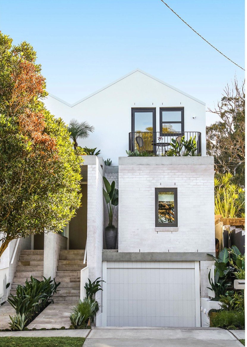White brick coastal residence exterior with olive tree and stone entry steps