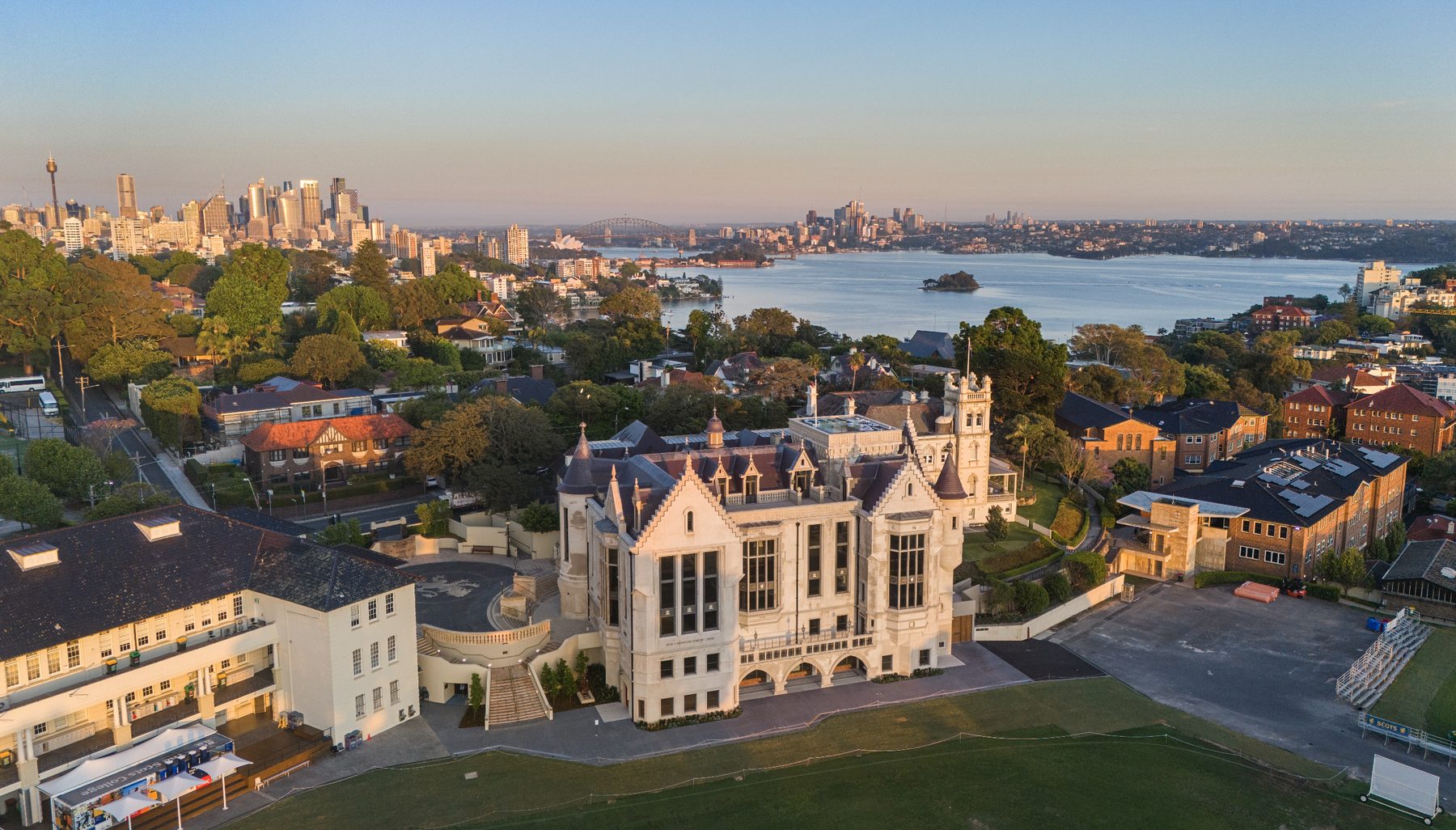 Wide golden hour aerial view of a heritage school building with Sydney harbour and skyline in the background