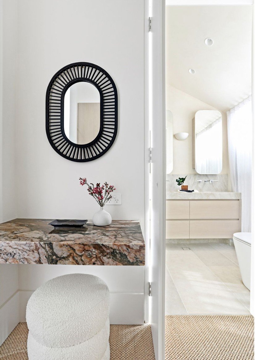 Powder room vanity with oval rattan-framed mirror and marble shelf