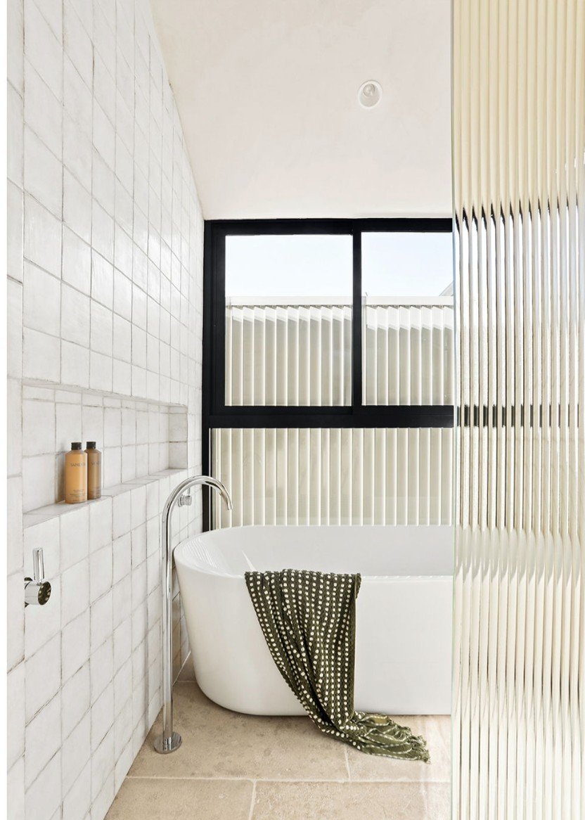 Freestanding bathtub with fluted glass screen, black-framed window and stone tiled walls