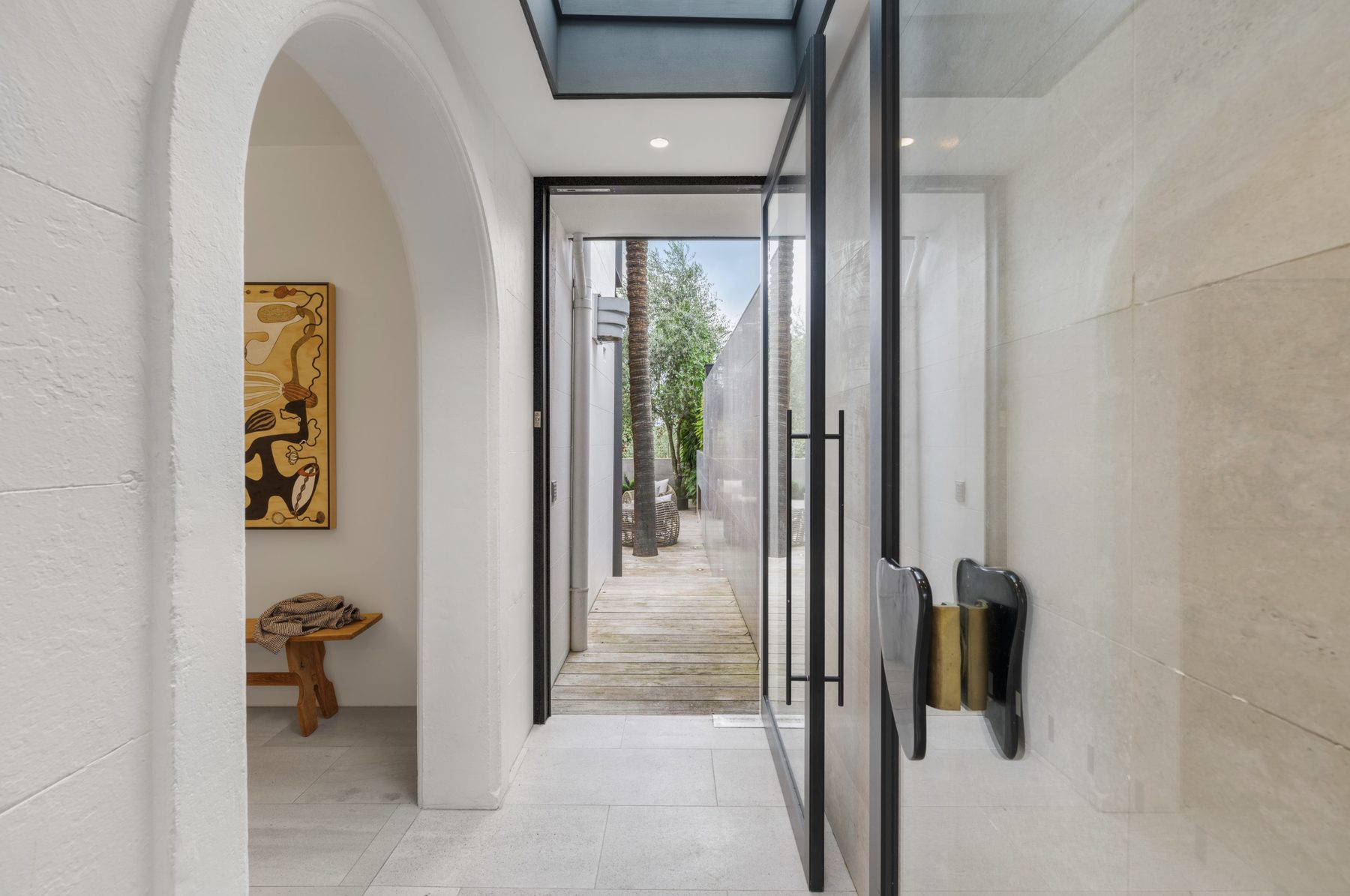 Arched hallway leading to a pivot glass door and timber deck